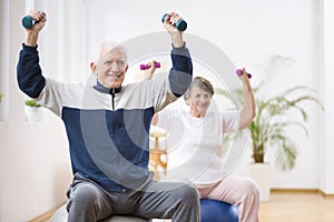 Elderly man and woman exercising on gymnastic balls during physiotherapy session at hospital