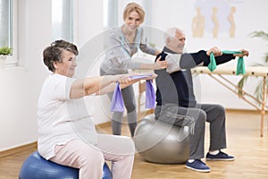 Elderly man and woman exercising on gymnastic balls during physiotherapy session at hospital