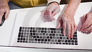 elderly man and woman having fun playing games on a laptop while sitting at a table in room, hands close-up