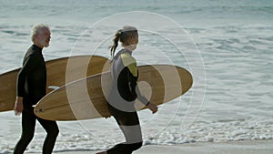 Elderly man and woman with surfboards running along sea shore