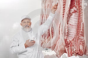 Man in uniform standing near row of pork carcasses, testing.