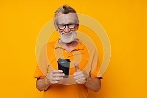 elderly man in a yellow T-shirt a glass with a drink yellow background