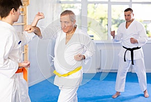 Elderly man and young guy sparring during karate classes in the gym under the guidance of coach