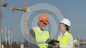 Elderly man and a young woman with a tablet in hands at a construction site. Builders discuss working issues.