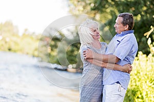 Elderly marriage hugging by the lake.