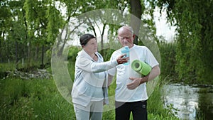 Elderly married couple with bottle of water for sports nutrition and yoga mat go hand in hand after playing sports and