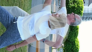 Elderly married couple is exercising doing yoga outdoors on the green lawn of the park at dawn.