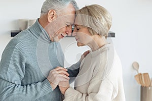 Elderly married couple hugging, standing together at home