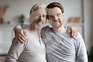 Elderly mature dad cuddling shoulders of grownup son.