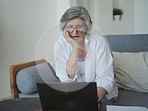 Elderly mature old serious woman working with laptop and paper, shocked by high taxes and retirement savings problems