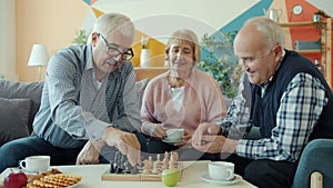 Elderly men playing chess at home while woman drinking tea relaxing at home