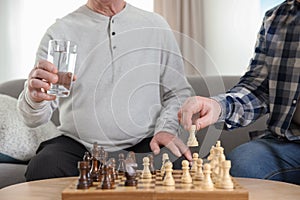 Elderly men playing chess at nursing home, closeup. Assisting senior