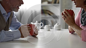 Elderly man and woman sitting at kitchen table, drinking tea, happy couple