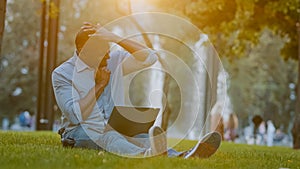 Elderly middle-aged African American businessman entrepreneur man sitting on grass in city park working on computer