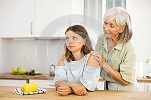Elderly mother asks for forgiveness from her adult daughter and calms her down after a domestic quarrel in kitchen
