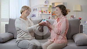 Elderly mother giving present to daughter sitting home sofa, relations closeness