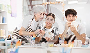 Elderly mother guiding young adult children painting pottery in family workshop