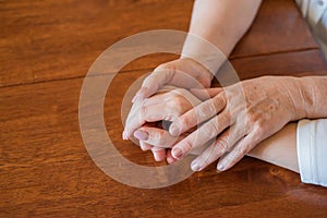 Elderly mother and her daughter holding hands while sitting at the table.Close up on women of different generations holding hands