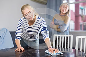Elderly mother is unhappy with the way her adult daughter dusts the table in room