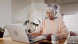 Elderly Multi-cultural woman making online purchase using laptop and credit card at home