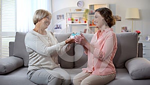 Elderly mum giving present to daughter sitting sofa at home, relations closeness photo