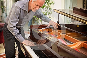 Elderly music instrument technician tuning a piano keyboard.