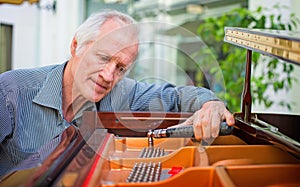 Elderly music instrument technician tuning a piano keyboard. photo