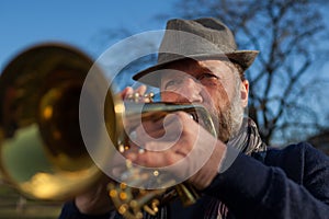 An elderly musician plays in the street on a trumpet