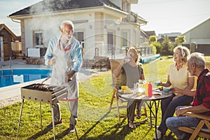 Elderly neighbors having backyard barbecue party by the pool