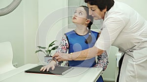 An elderly nurse is preparing a little girl for X-ray brushes.