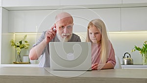 Elderly old grandfather, along with blonde granddaughter, asks and learns how to use computer applications. Focused