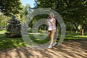 Elderly old woman having online video call with relatives while walking in park