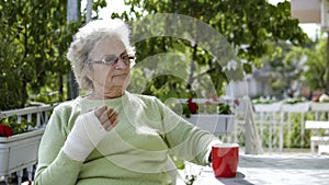 Elderly old woman with injured hand drinking coffee