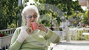 Elderly old woman with injured hand drinking coffee outdoor