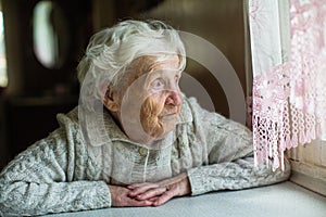 An elderly old woman looks sadly out the window.