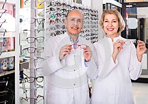 Elderly opticians helping to choose glasses in modern optics store