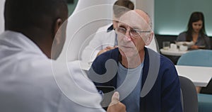 Elderly patient sits in clinic cafe with African American doctor