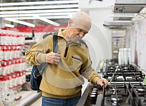 Elderly pensioner looks at a gas stove on the counter in a store