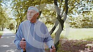 Elderly pensioner old man grandfather training Nordic walking use ski trekking poles in summer park