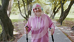 Elderly pensioner old woman grandmother training Nordic walking use ski trekking poles in sunny park