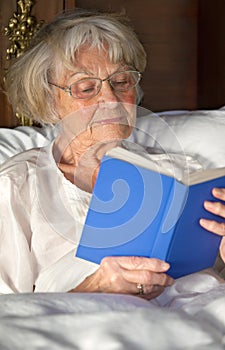 Elderly pensioner reading a book in bed