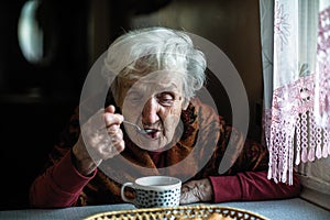 An elderly pensioner woman drinking tea at home.