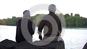 Elderly pensioners enjoying forest and water sitting on river bank, weekend rest