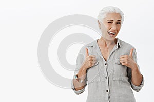 Elderly people can rock too. Portrait of charming enthusiastic granny with grey hair in loose shirt showing thumbs up in