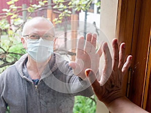 Elderly people in medical masks communicate through the window glass. New realities of communication in the world