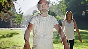 Elderly People In Park Go In For Sports. Elderly Gray Haired Man And Woman Squat With Arms Outstretched.