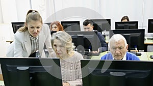 elderly people working on computers with young female teacher while attending pc class