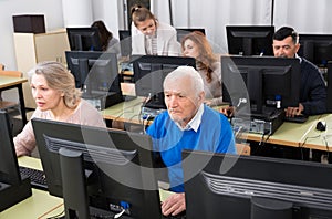 Elderly people working on computers with young teacher