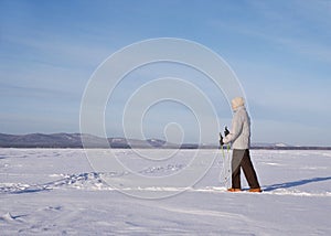 Elderly person alone doing Nordic walking in winter sunny day on a snow-covered lake, outdoor, side view.