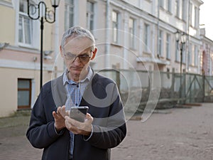 Elderly person is holding a mobile phone in his hands. Senior man is texting on smartphone. Old man is using cellphone